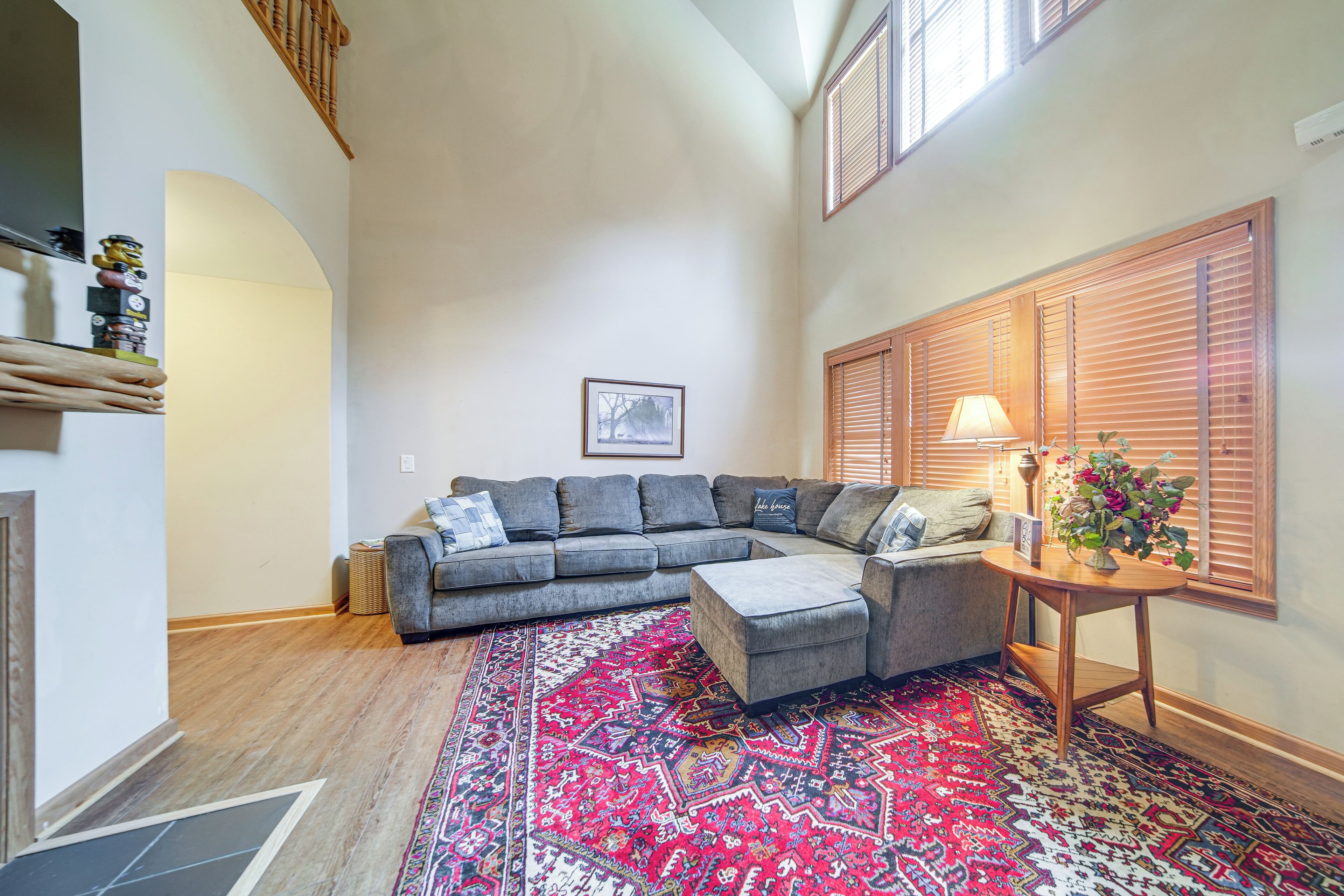 A living room with a sectional sofa, a patterned rug, a side table with a lamp, and a window with blinds.