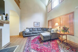 A living room with a sectional sofa, a patterned rug, a side table with a lamp, and a window with blinds. - Conneaut Lake Home With Yard, 1/2 Mi to Beach/park (Conneaut Lake)