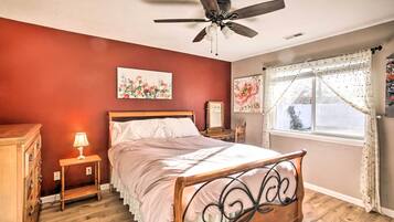 A bedroom with a wooden bed, a ceiling fan, a nightstand with a lamp, and floral artwork on the walls.
