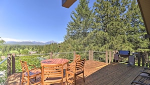 Une terrasse en bois avec une table ronde et des chaises, un barbecue et une vue sur les montagnes et les arbres.