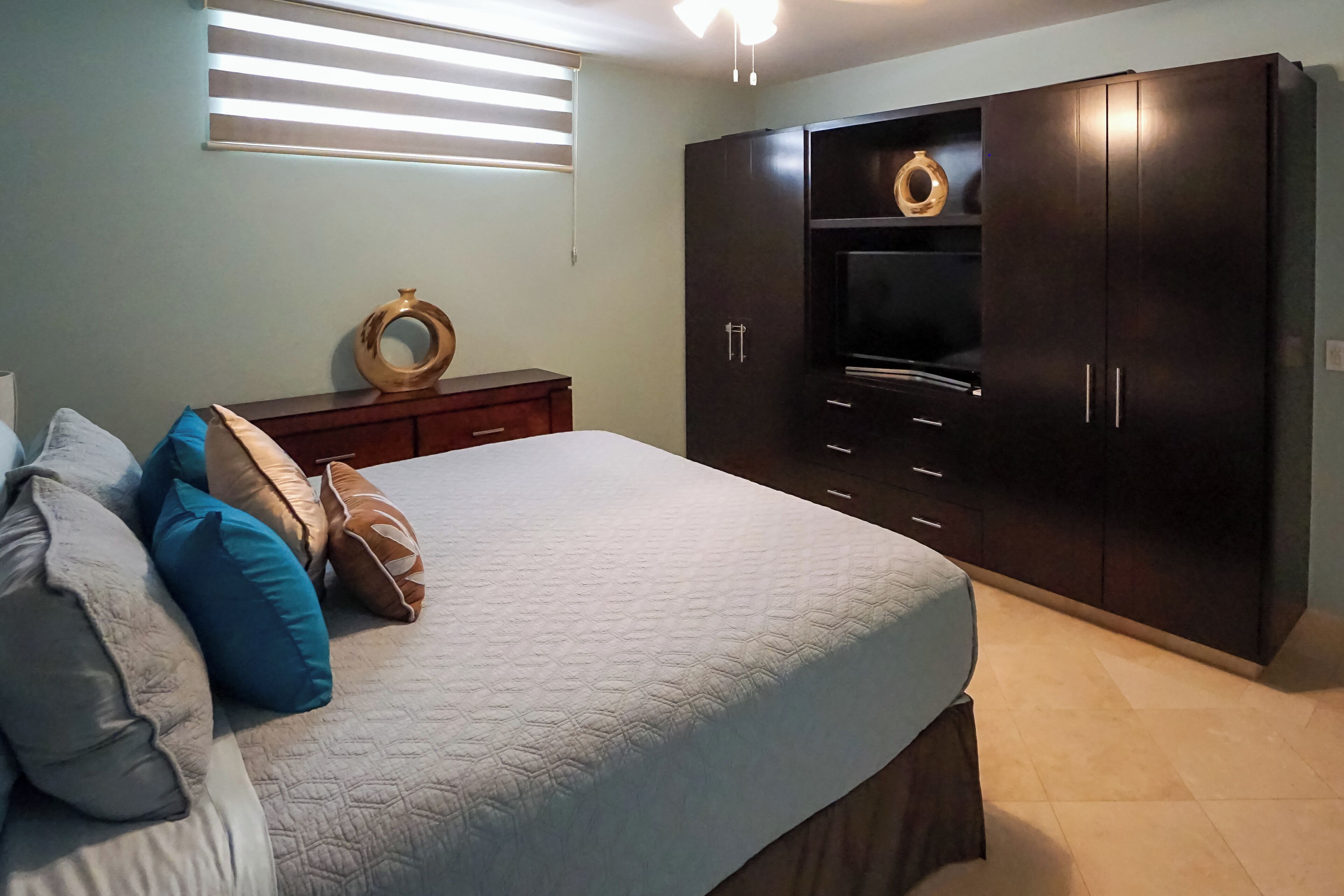 A bedroom with a bed, pillows, a dresser, a TV, and a wardrobe.