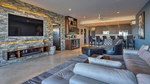Een moderne woonkamer met een accentmuur van steen, een grote flatscreen-tv, een leren bank en een eethoek met een bar.