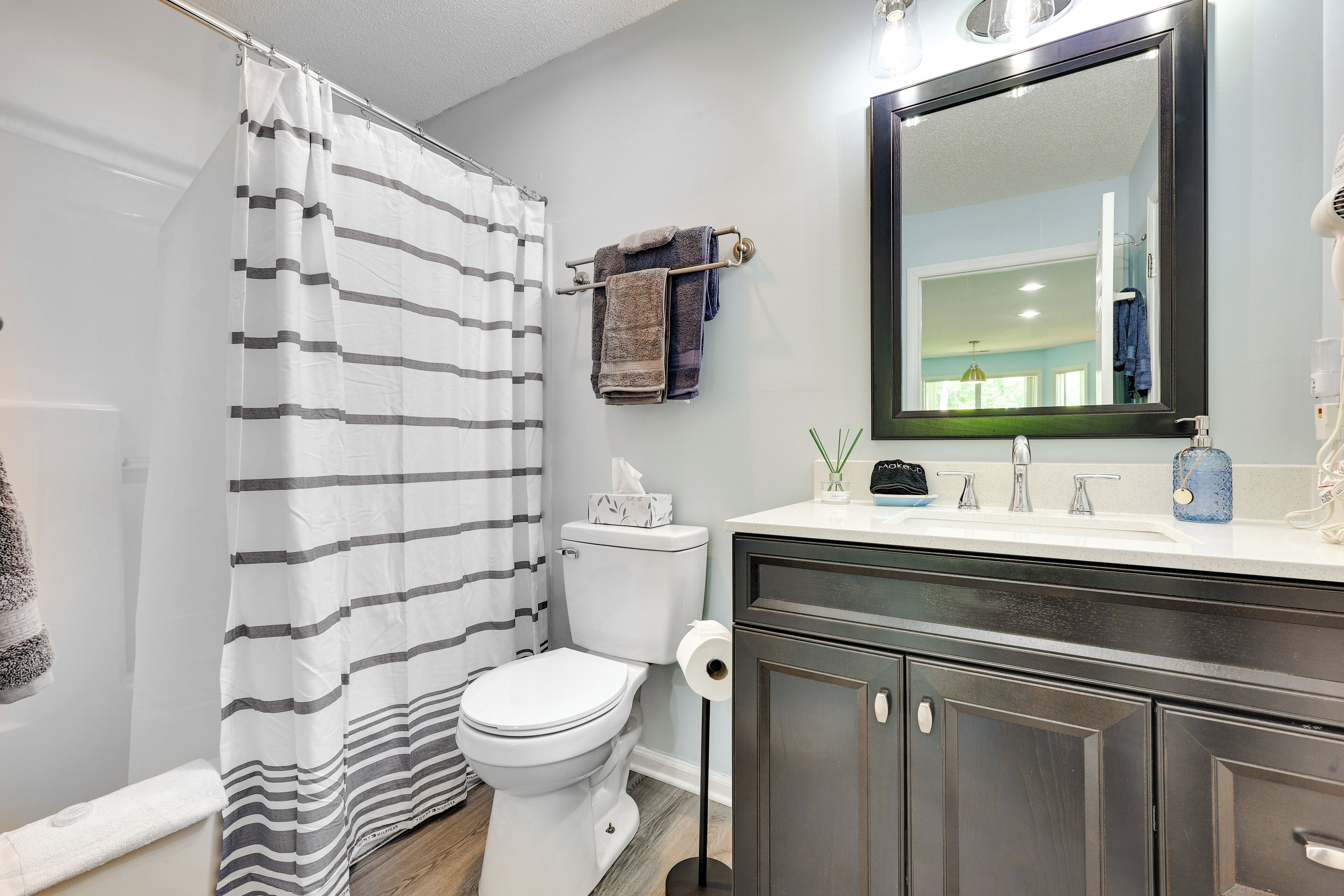 A bathroom with a striped shower curtain, a toilet, a sink with a mirror, and a towel rack with towels.