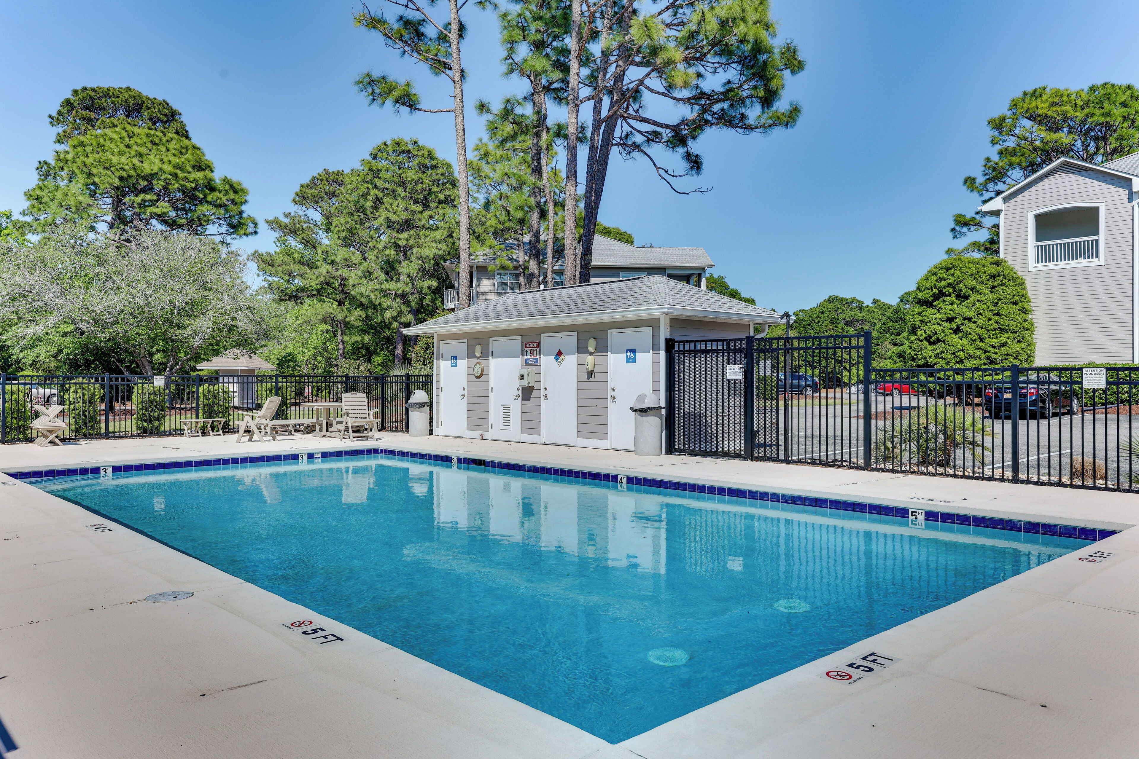 A rectangular swimming pool with a tiled edge, surrounded by a fence, and adjacent to a building with a balcony.