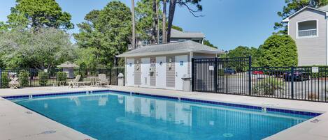 A rectangular swimming pool with a tiled edge, surrounded by a fence, and adjacent to a building with a balcony.
