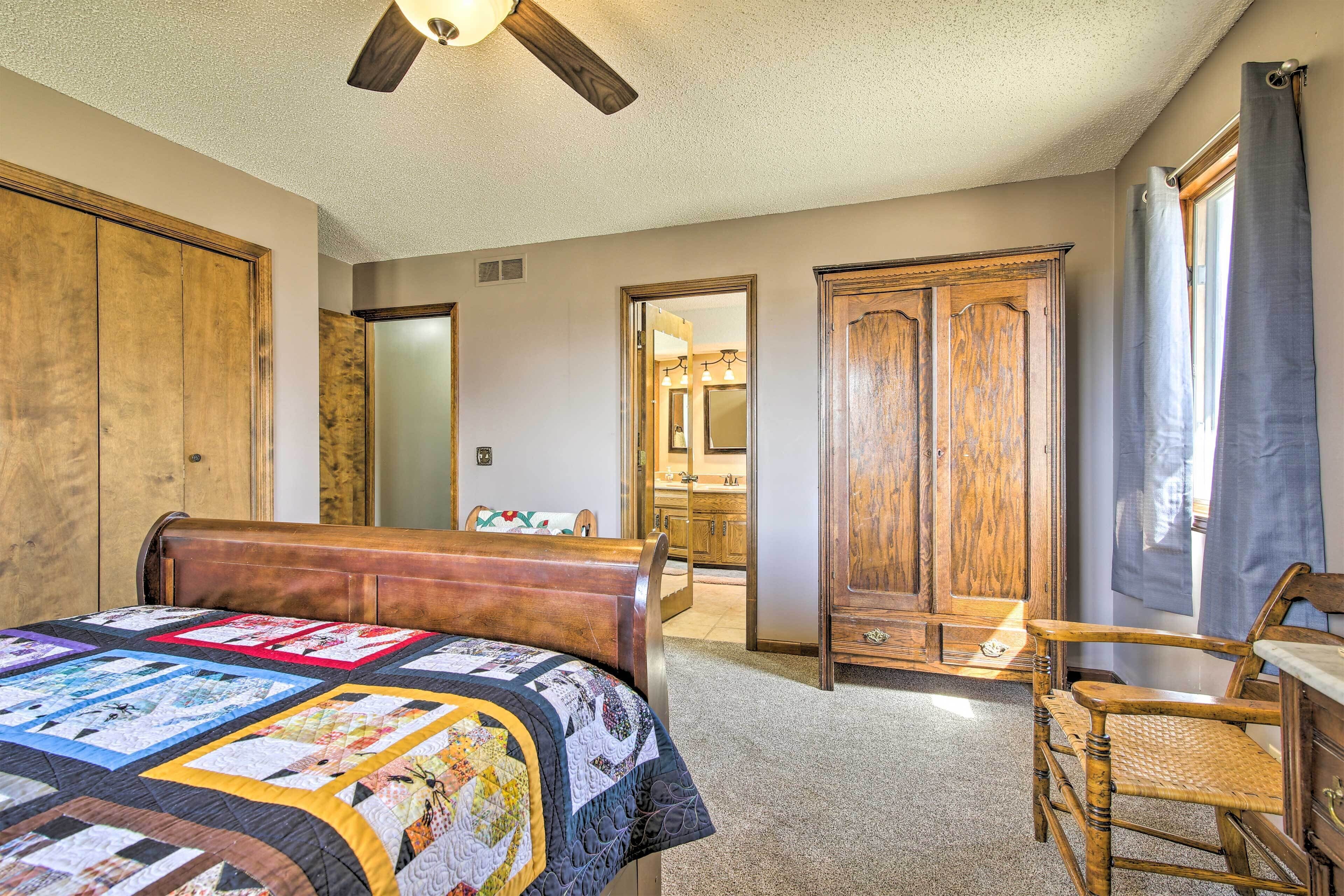 Une chambre à coucher avec un lit en bois, une courtepointe, une chaise en bois et un ventilateur de plafond.