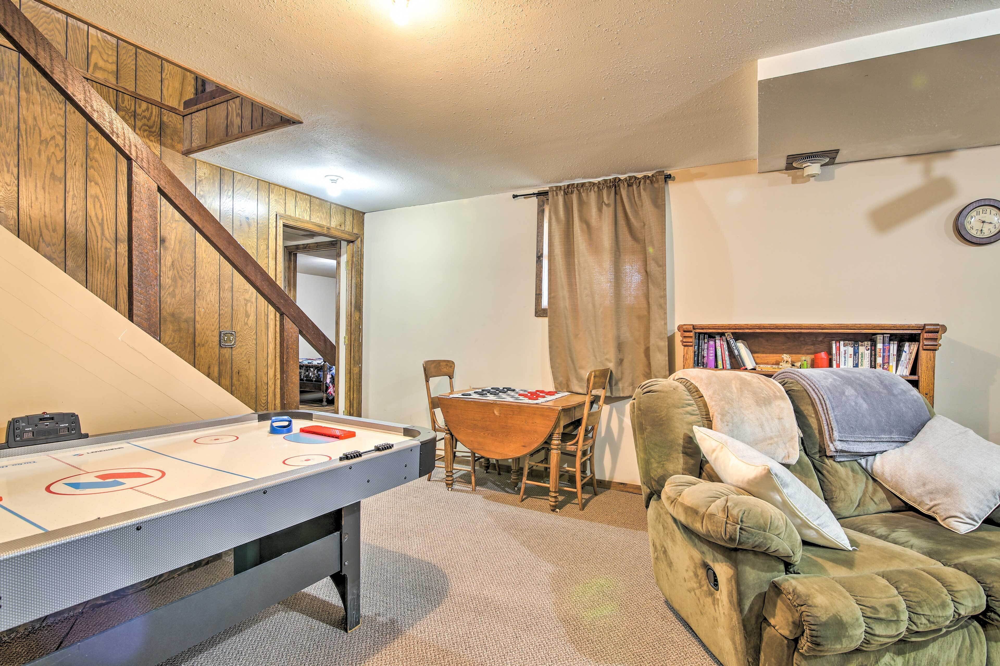 A cozy living room with a pool table, a green sofa, a wooden staircase, and a bookshelf.