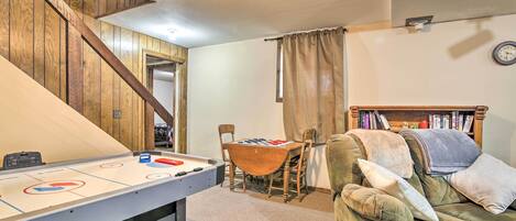 A cozy living room with a pool table, a green sofa, a wooden staircase, and a bookshelf.