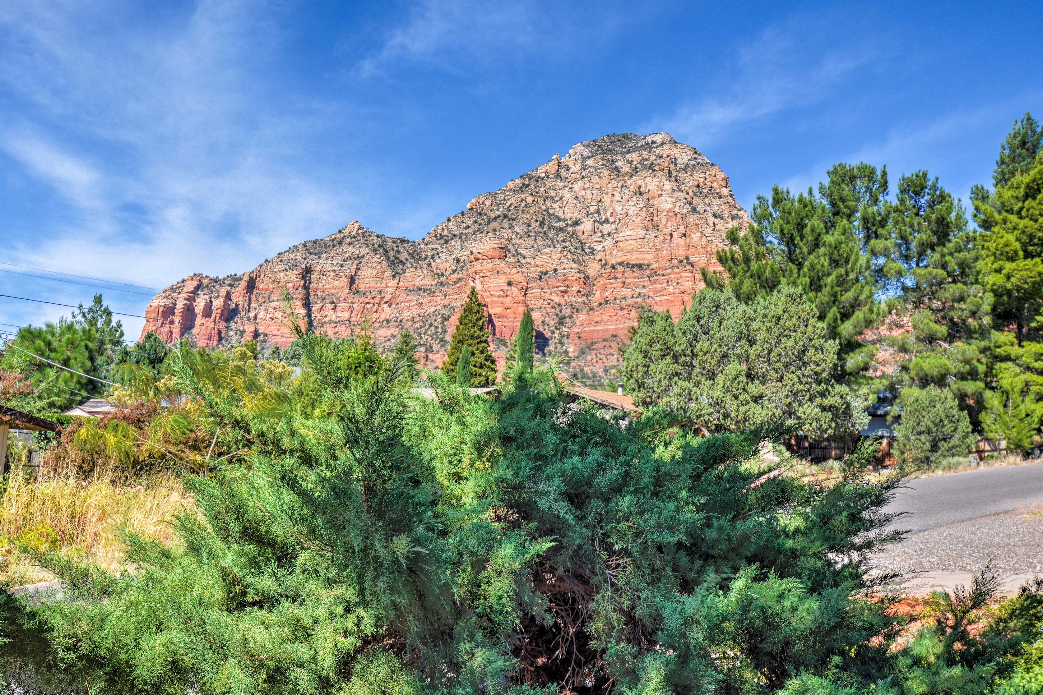 Un paisaje montañoso con un pico rocoso destacado, rodeado de densa vegetación verde y un cielo azul despejado.