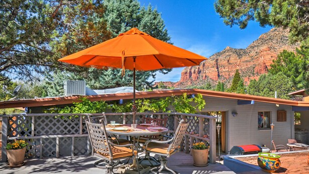 An outdoor patio with a table and chairs, an orange umbrella, and a view of red rock formations. - Patio & Views: Peaceful Sedona Getaway! (Sedona)