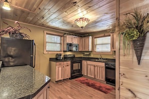 A kitchen with wooden cabinets, a granite countertop, a refrigerator, a stove, and a microwave. - Hot Tub & Loft: Mountain-view Sevierville Cabin (Sevierville)