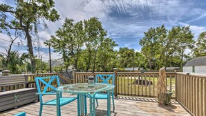 A wooden deck with a glass table and blue chairs, surrounded by a wooden fence and trees.