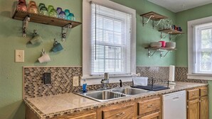 A kitchen with a double sink, wooden cabinets, a dishwasher, and a tiled backsplash.