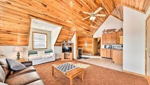A spacious living room with a wooden ceiling, a fireplace, a sofa, a coffee table, and a kitchen area with wooden cabinets and appliances. - Ski-in/ski-out Ghent Cabin w/ Mountain Views! (Ghent)