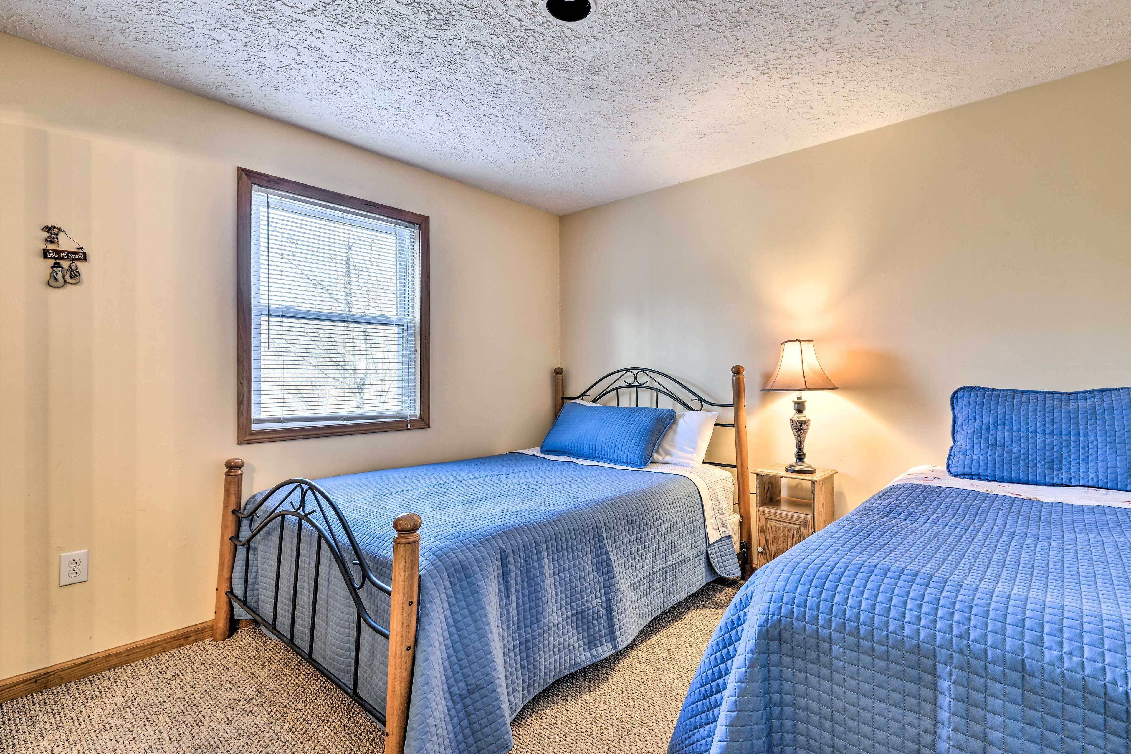 A bedroom with two beds, a window, a nightstand, and a lamp.