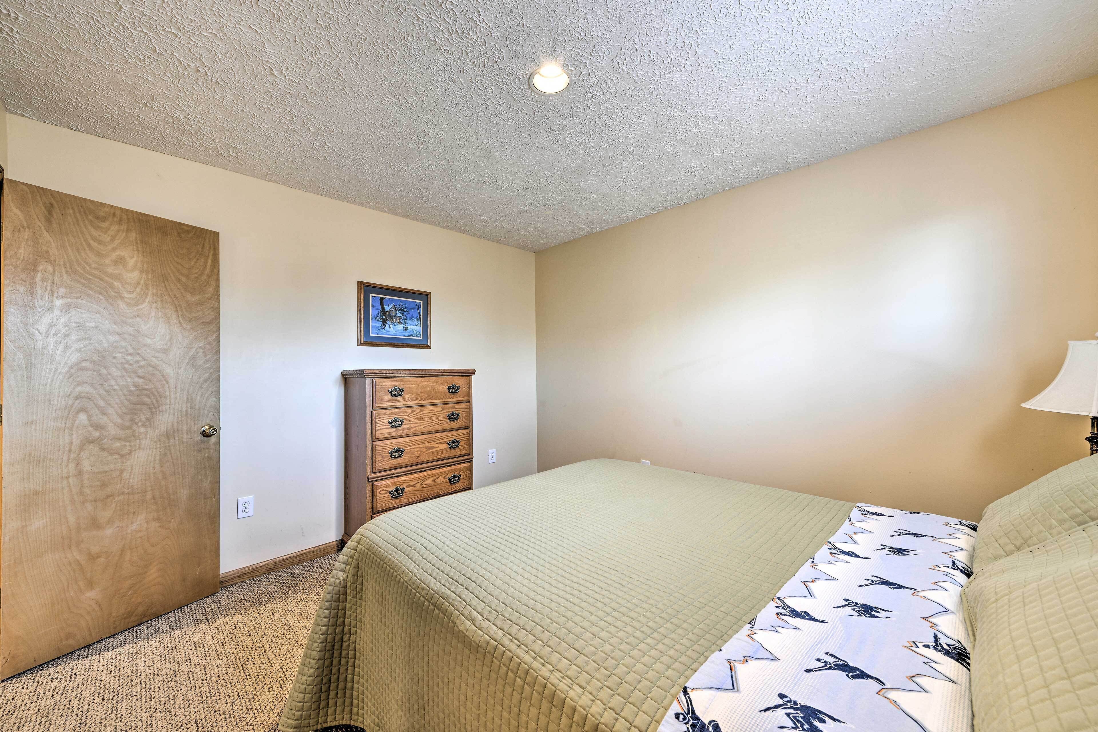 Une chambre à coucher avec un lit, une commode en bois, un tableau encadré au mur et un luminaire au plafond.