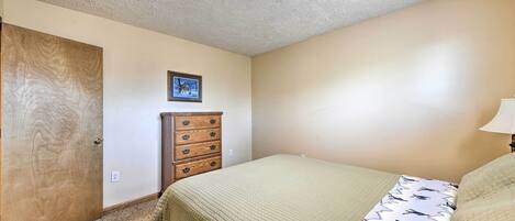 A bedroom with a bed, a wooden dresser, a framed picture on the wall, and a ceiling light.