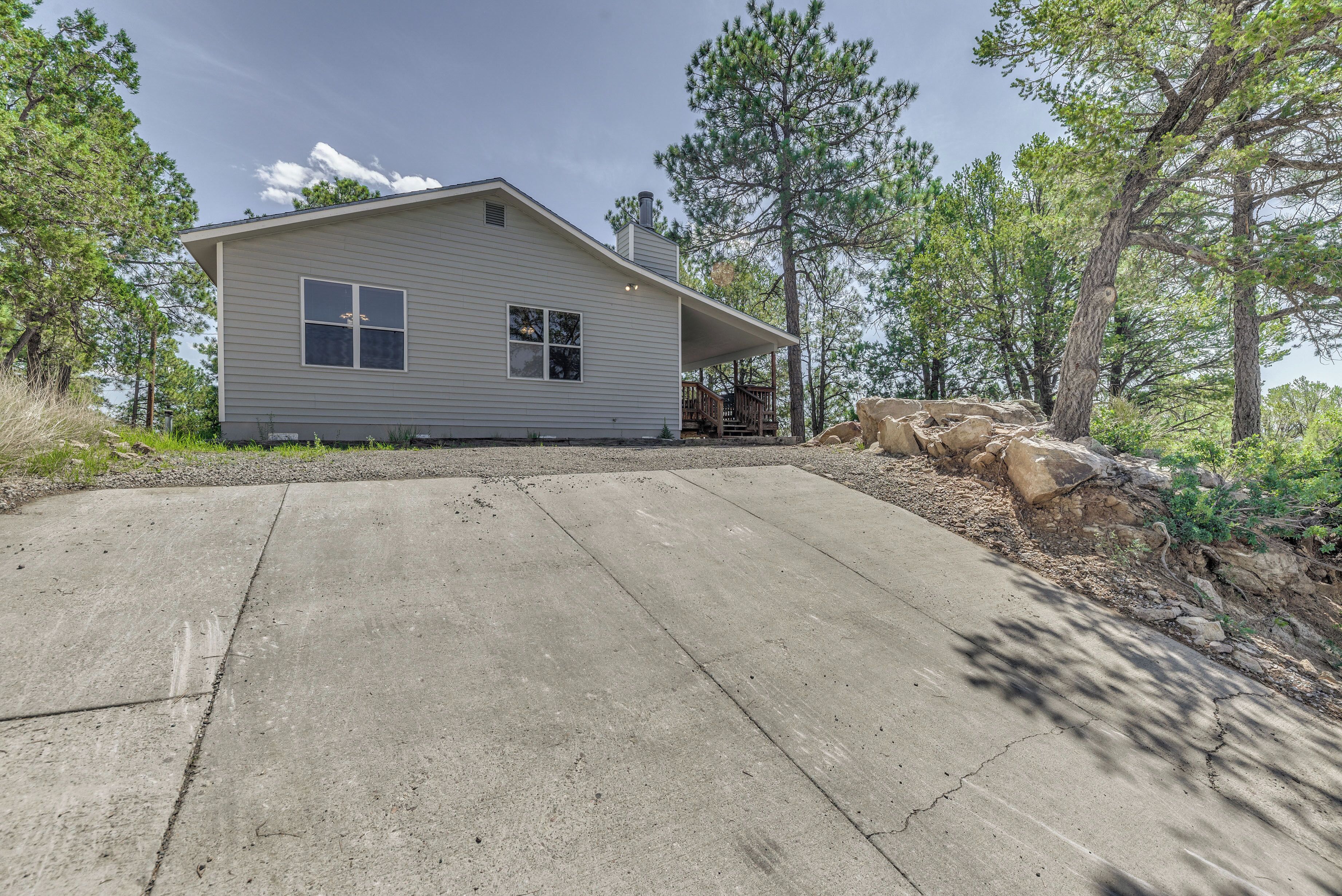 A single-story house with a covered porch, surrounded by trees and a rocky landscape.