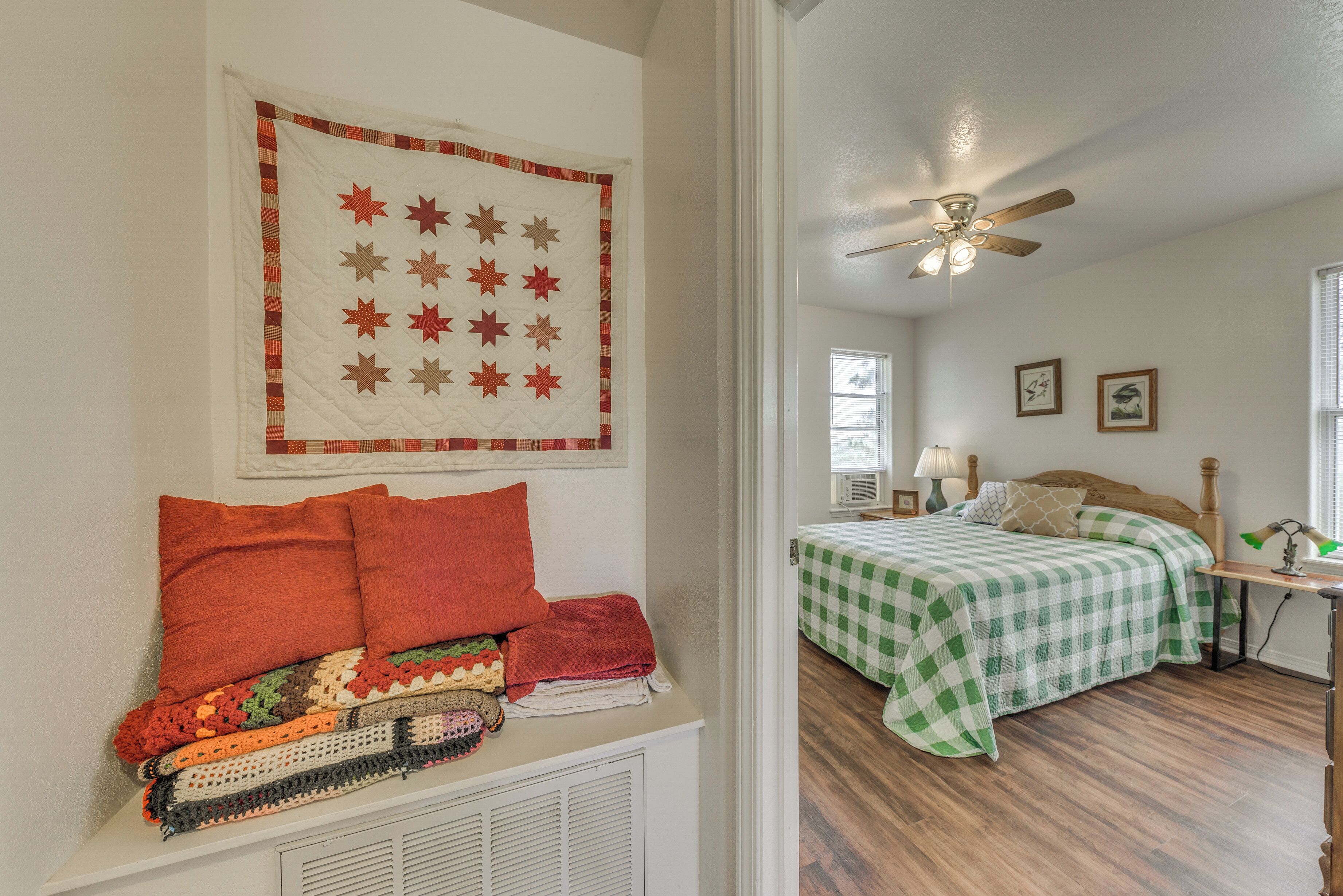 A bedroom with a bed, a ceiling fan, and a quilt hanging on the wall.