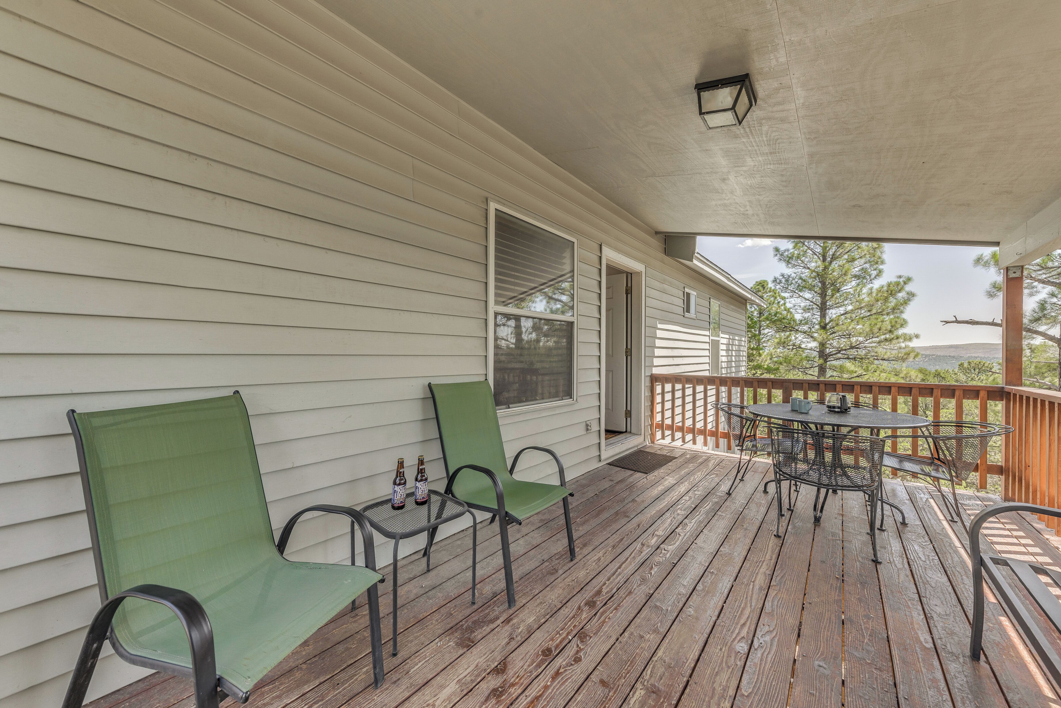 A wooden deck with a table and two chairs, a small table with bottles, and a view of trees and hills.