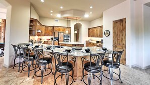 A spacious kitchen with a central island, wooden cabinets, and black metal chairs. - Scottsdale Home: Pickleball, Heated Pool & Hot Tub (Scottsdale)