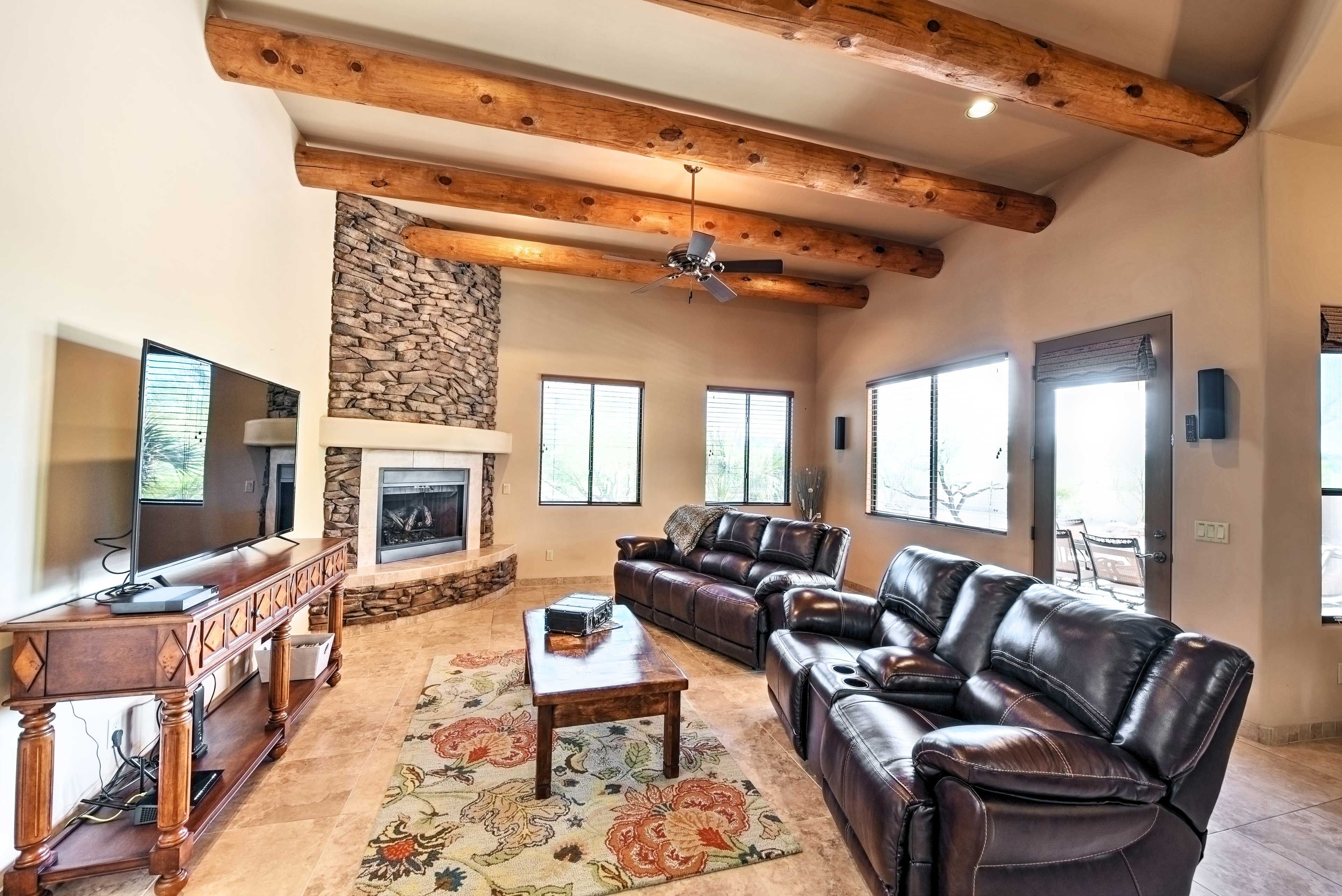 A spacious living room with a stone fireplace, leather sofas, a wooden coffee table, and a television on a wooden stand.