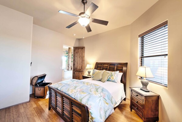 Een slaapkamer met een houten bed, een plafondventilator, een nachtkastje met een lamp en een raam met jaloezieën.
