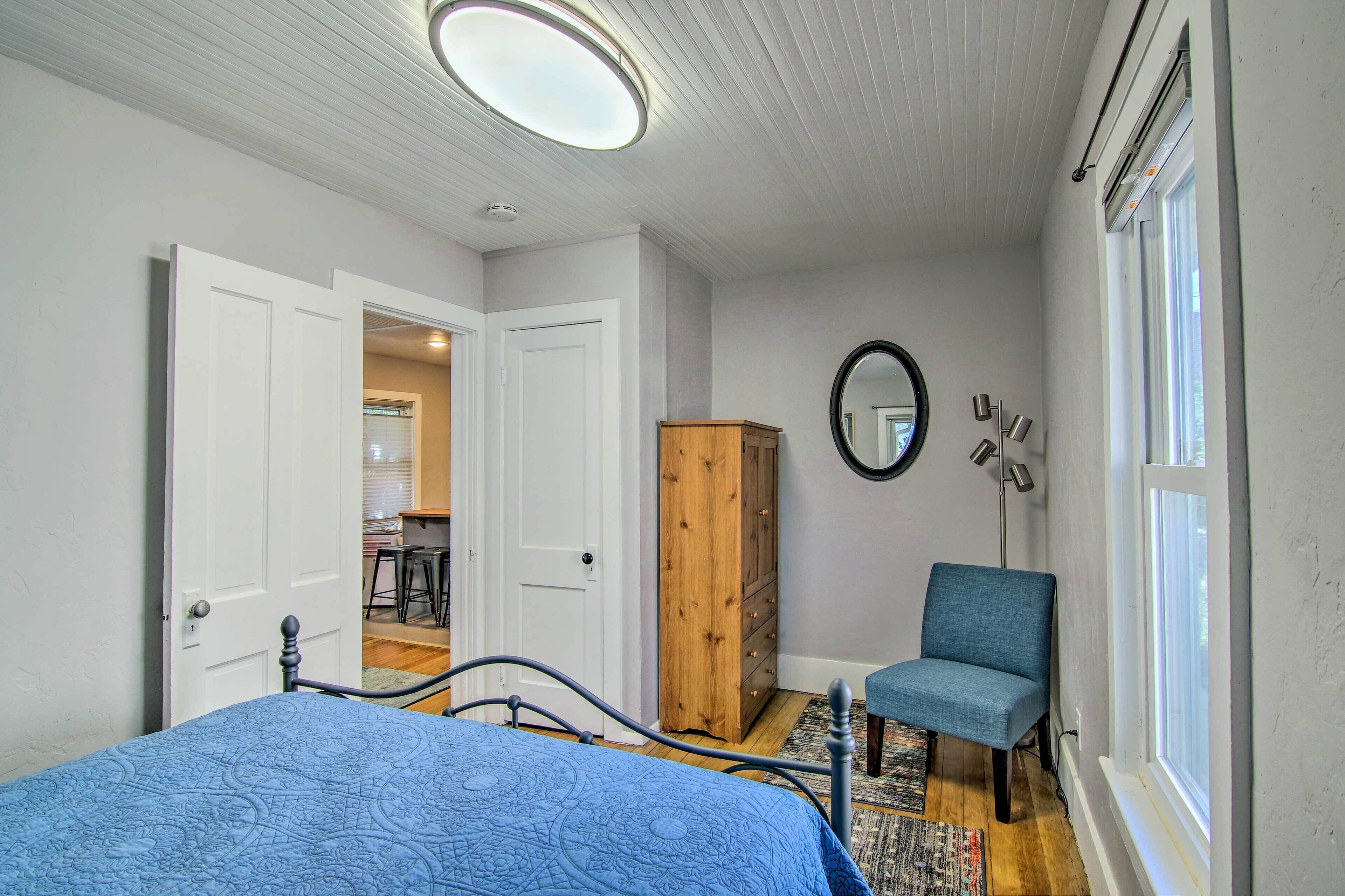 Une chambre à coucher avec un lit, une chaise, une armoire, un miroir et une fenêtre.
