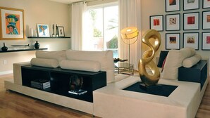 Uma sala de estar moderna com um sofá branco, um móvel de entretenimento preto e uma grande escultura dourada.