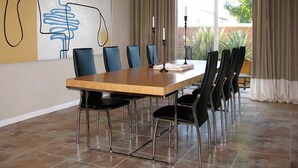 Uma sala de jantar com uma mesa retangular, seis cadeiras e um grande quadro abstrato na parede.
