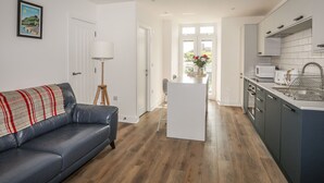 A modern kitchen with white cabinets, a dining area with a white table, and a blue leather sofa. - Swn Y Mor / Sound of the Sea (Criccieth)