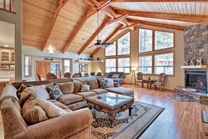 A spacious living room with a high ceiling, large windows, a fireplace, and a cozy seating area. - Sand Volleyball & Deck: Munds Park Getaway! (Munds Park)