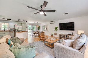 A modern living room with a sofa, coffee table, and a TV. There is a dining area with chairs and a table, and a kitchen in the background. - Family-friendly Saugerties Home w/ Hot Tub & Games (Saugerties)
