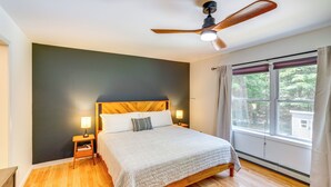 Une chambre à coucher avec un lit en bois, deux tables de chevet avec des lampes, un ventilateur de plafond et une fenêtre avec des rideaux.