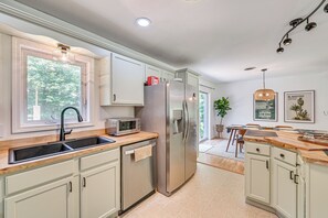 A modern kitchen with a stainless steel refrigerator, a built-in oven, and a sink. There is a window providing natural light and a view of greenery outside. - Family-friendly Saugerties Home w/ Hot Tub & Games (Saugerties)