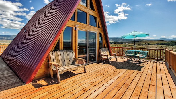 Un terrazzo in legno con due sedie e un tavolo, un ombrellone e vista sul paesaggio.