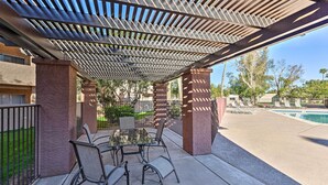 Um pátio externo com mesa, cadeiras, piscina e uma estrutura de pérgola.