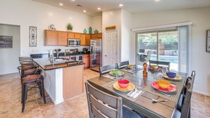A modern kitchen with a central island, wooden cabinets, and a dining area with a glass table and chairs. - Backyard Oasis: Updated San Tan Valley Escape (San Tan Valley)