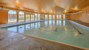 An indoor swimming pool with wooden ceiling and large windows.