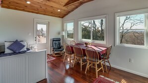 Un comedor con techo de madera, una mesa de comedor con sillas y ventanas grandes con vistas a árboles.