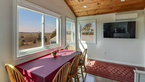 Un comedor con mesa y sillas, ventanas amplias con vistas al exterior, un ventilador de techo y un televisor montado.