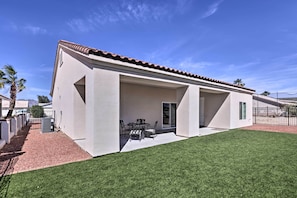 Ein modernes Haus mit überdachter Terrasse, Rasenfläche und blauem Himmel.