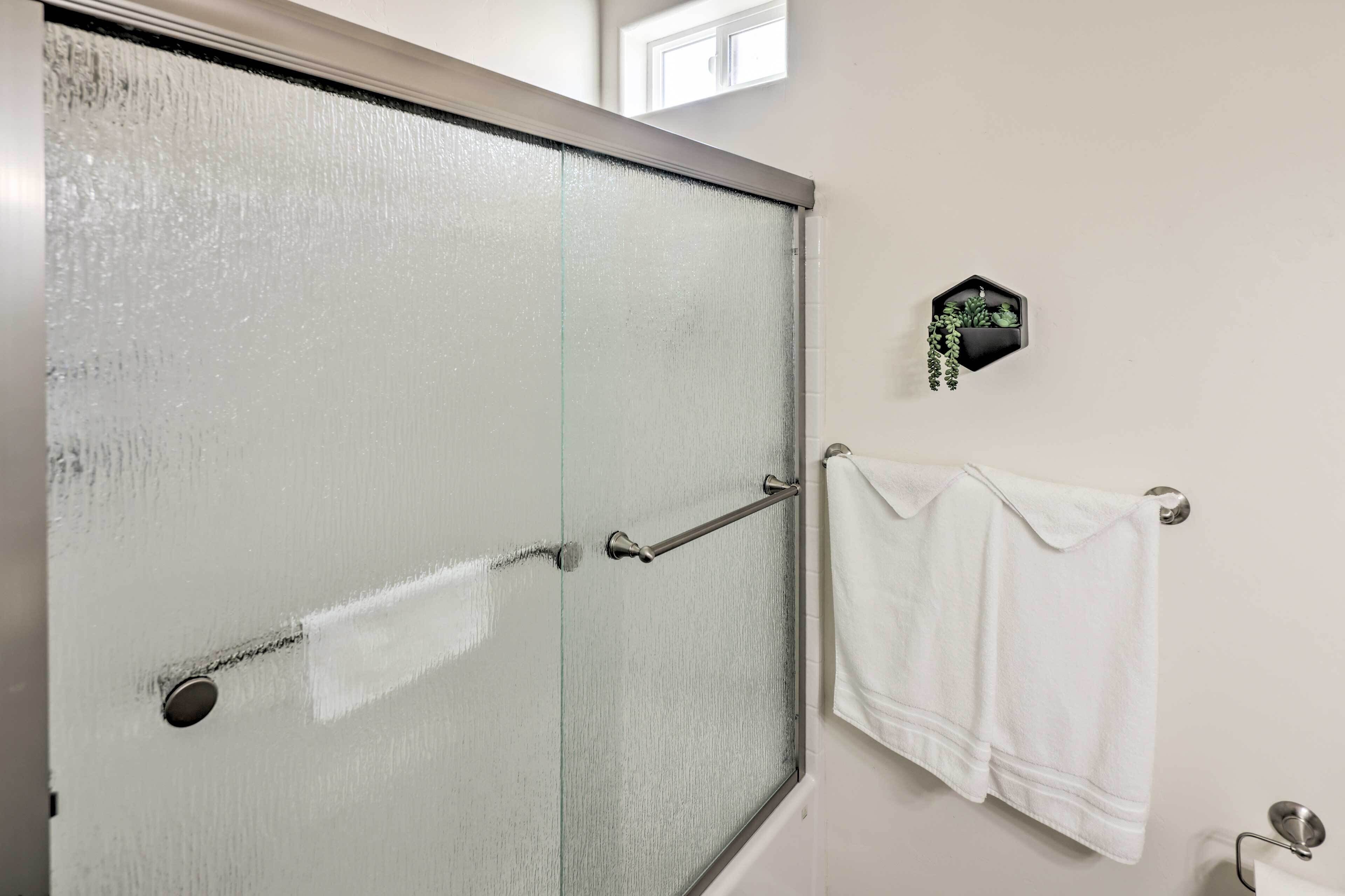 Une salle de bain avec une porte de douche en verre dépoli, un porte-serviettes avec deux serviettes blanches et une petite plante en pot accrochée au mur.