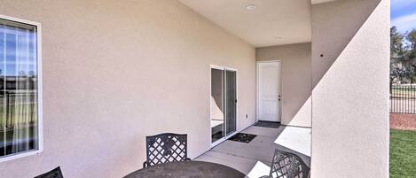 A covered patio area with a round table and four chairs, a sliding glass door, and a white door.