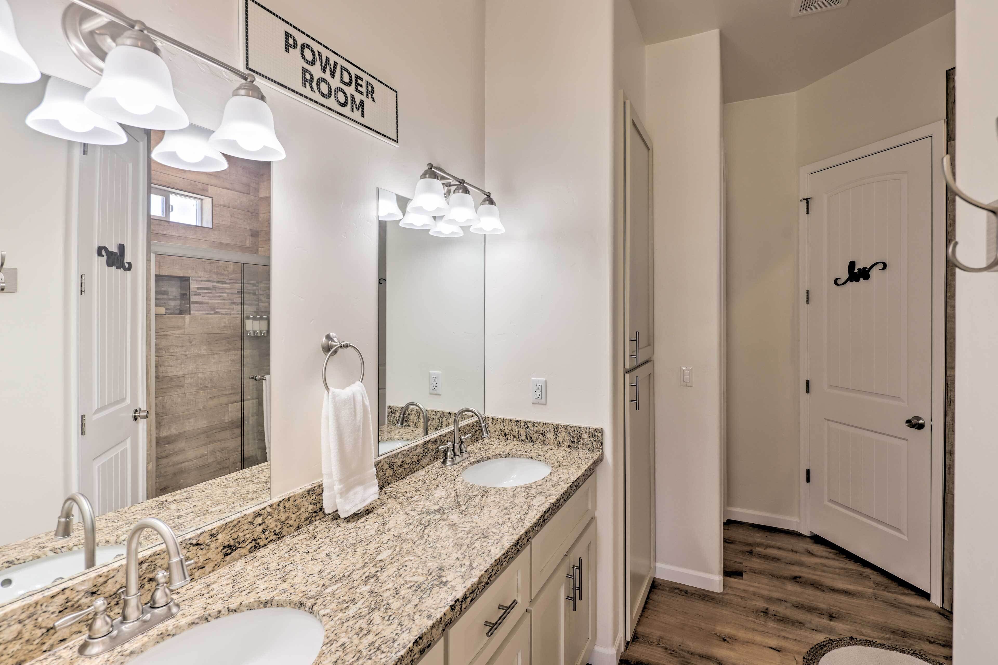 Une salle de bain avec un comptoir en granit, deux lavabos, un grand miroir et une pancarte indiquant « TOILETTES ».
