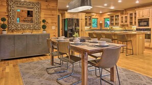A modern kitchen with wooden cabinets, a central island, and a dining area with a table and chairs. - 7 Mi to Ski Slopes: Mars Hill Cabin w/ Hot Tub! (Mars Hill)