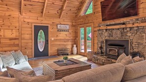 A cozy cabin interior with a stone fireplace, wooden walls, a large TV, and a comfortable seating area. - 7 Mi to Ski Slopes: Mars Hill Cabin w/ Hot Tub! (Mars Hill)