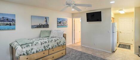 A bedroom with a bed, a ceiling fan, a TV mounted on the wall, and a door leading to another room.