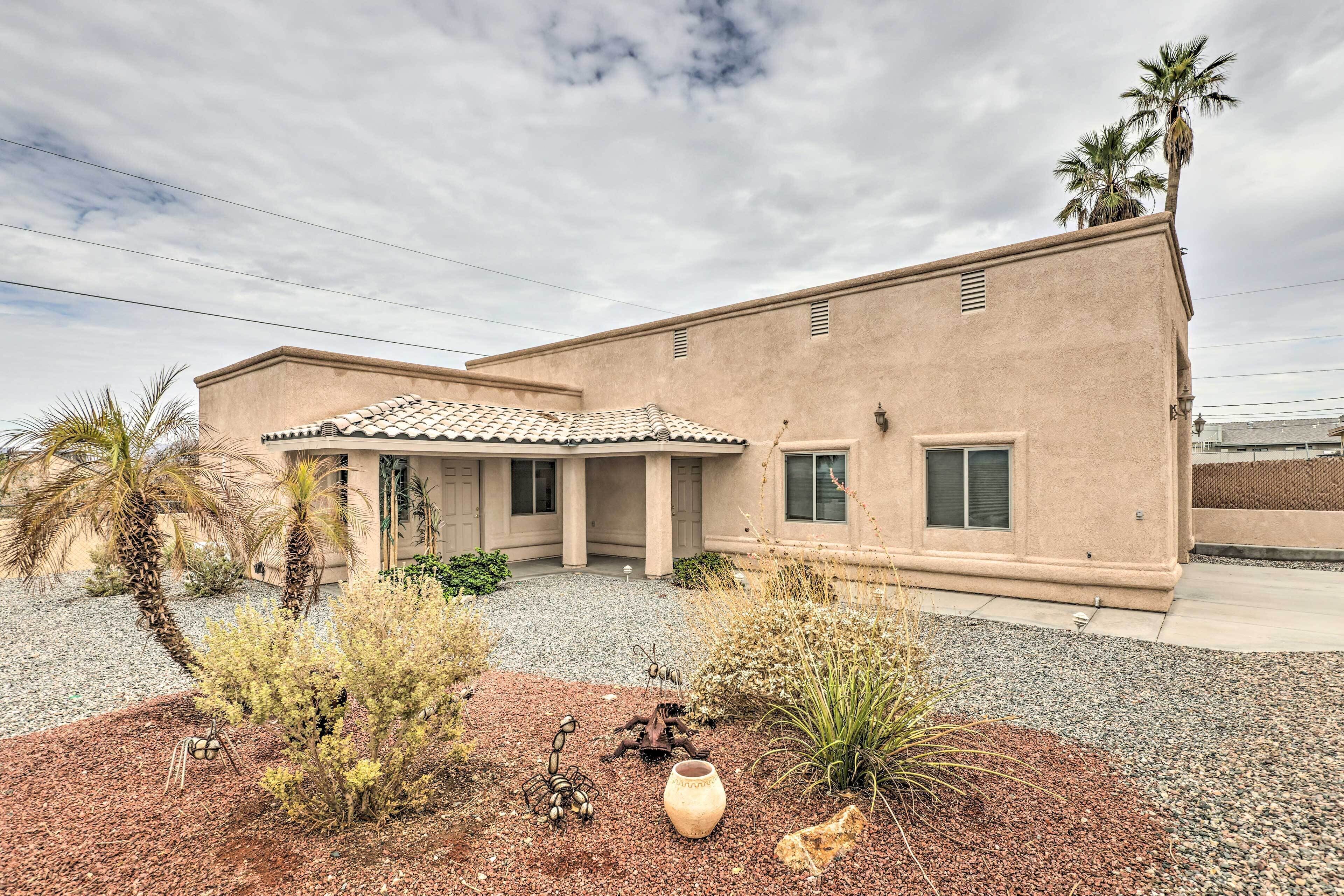 A stucco building with a tiled roof, a gravel driveway, and a small garden with plants and a decorative vase.