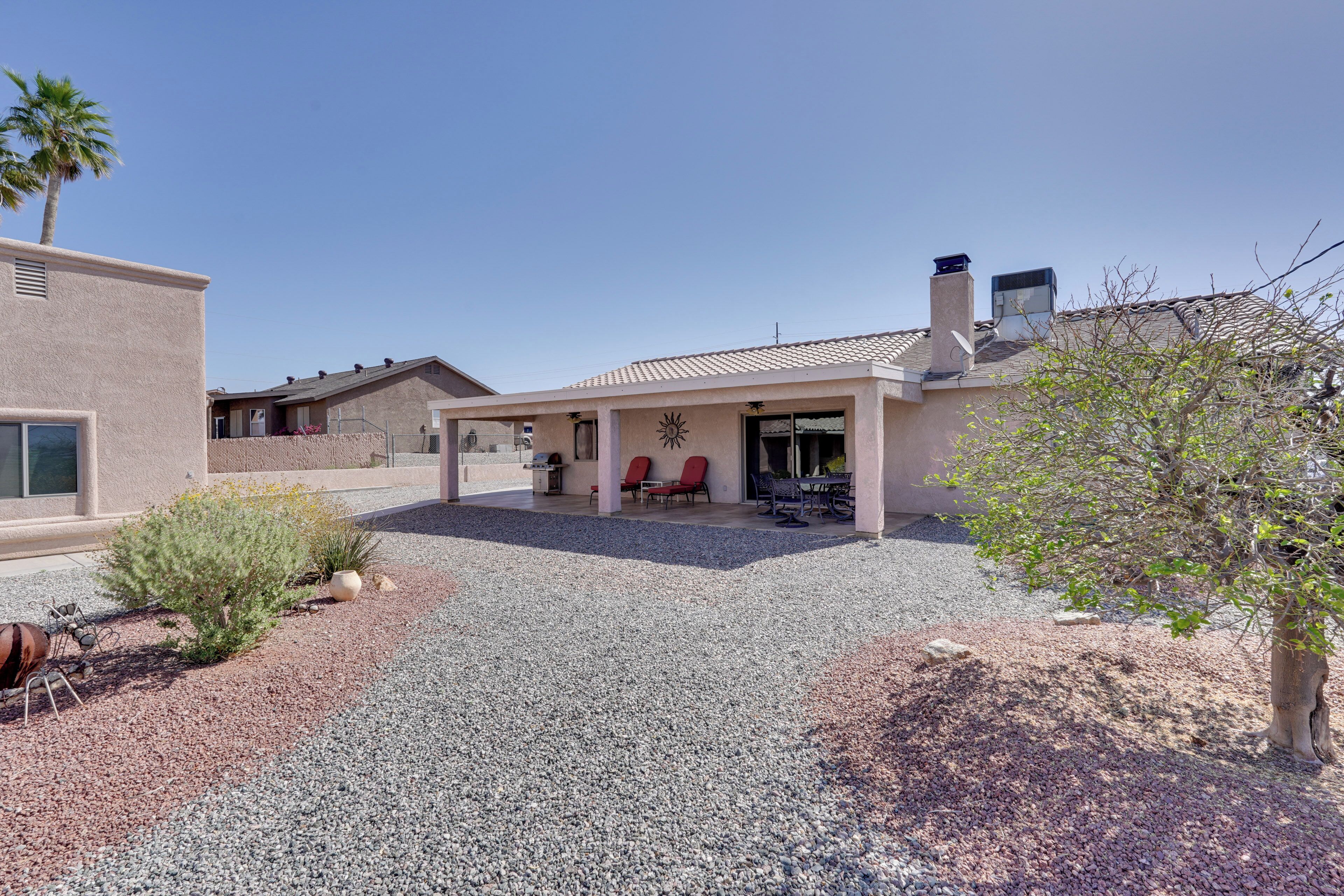 A house with a patio area, a gravel driveway, and a small garden with a palm tree and a cactus.